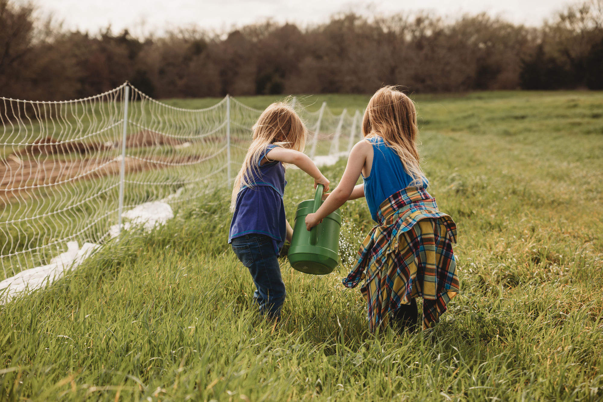 Two girls watering plants together in the field